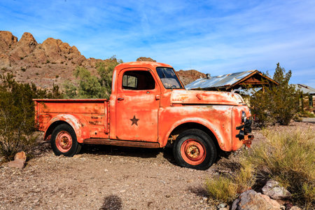 An old rusty red truck is parked in a desert. The truck is covered in rust and has a star on the hood. The desert landscape is barren and desolate, with no signs of lifeの写真素材