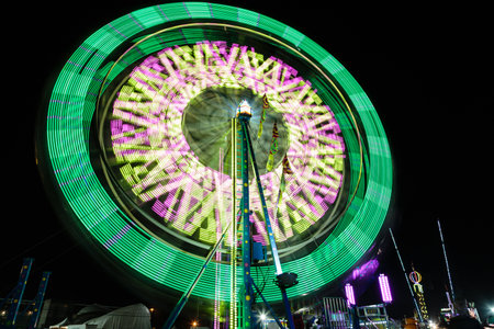 A colorful merry go round with lights on it is spinning in the dark. The lights are green and purple, creating a festive and lively atmosphereの写真素材