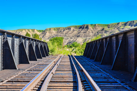 The train tracks are old and rusty, and the bridge is made of metal. The view of the mountains in the background is breathtakingの写真素材