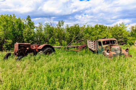 An old tractor and a truck are sitting in a field of grass. The tractor is rusted and the truck is old and broken. The scene gives off a feeling of abandonment and neglectの写真素材