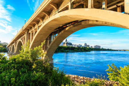 A bridge over a river with a city in the background. The bridge is a large arch and the water is calmの写真素材