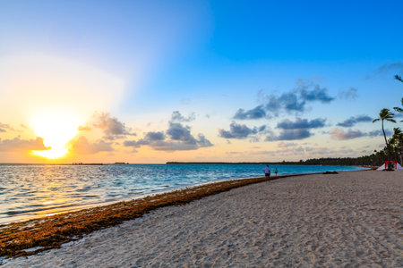 A beautiful beach with a clear blue ocean and a few people enjoying the sunset. The sky is filled with clouds, creating a serene and peaceful atmosphereの写真素材