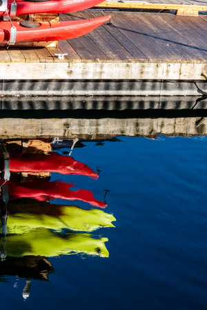 A row of red and yellow kayaks are reflected in the water. The kayaks are tied to a dockの写真素材