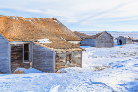 A small, run down house sits in the snow. The house is surrounded by other small houses, and the area is mostly empty. Scene is one of loneliness and isolationの写真素材