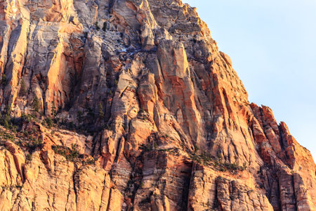 A mountain with a rocky surface and a clear blue sky. The mountain is covered in trees and has a rocky surfaceの写真素材