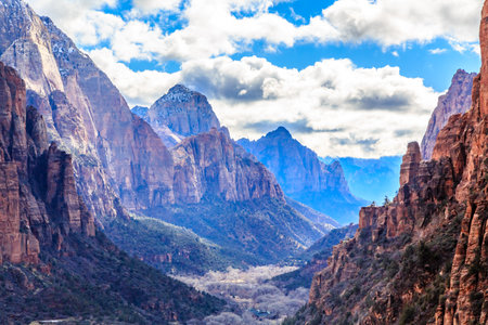A mountain range with a valley in between. The sky is blue and the mountains are covered in snowの写真素材