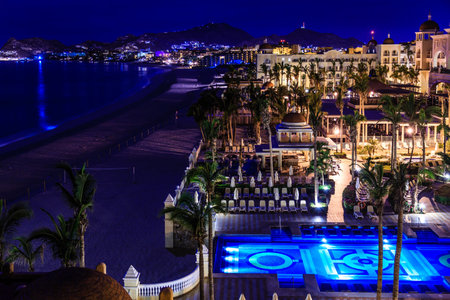 A beach with a hotel and pool at night. The pool is lit up and the hotel is lit up as wellの写真素材