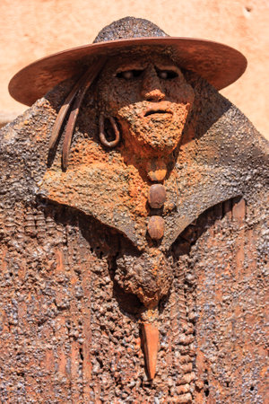 A man with a hat and a beard is carved out of wood. The man has a knife in his hand.の写真素材