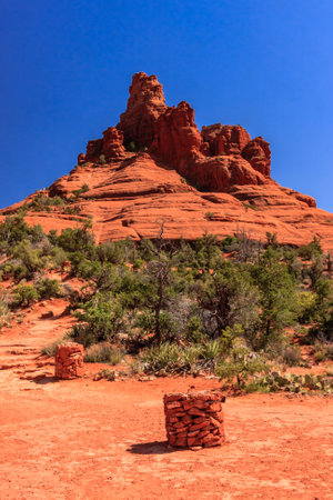 A mountain with a red rock on top and a blue sky in the background. The mountain is surrounded by a desert landscapeの写真素材