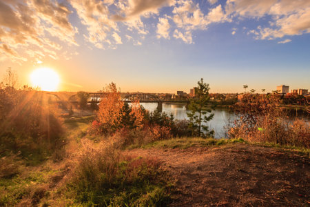 A beautiful sunset over a river with a bridge in the background. The sky is filled with clouds, and the sun is shining brightly. The scene is peaceful and sereneの写真素材