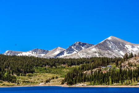 A mountain range with a clear blue sky and a lake in the background. The mountains are covered in snow and the trees are green. The scene is peaceful and sereneの写真素材