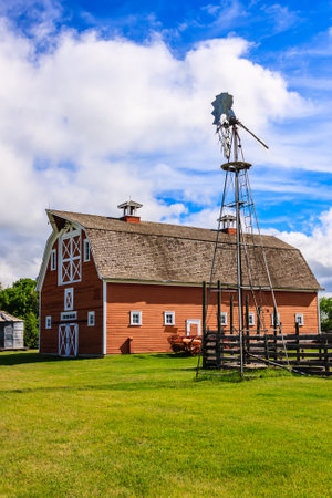 A red barn with a windmill on top. The barn is surrounded by a lush green field