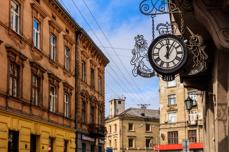 A clock hanging on a building with a lion on it. The clock is black and white. The building is brown and has many windowsの写真素材