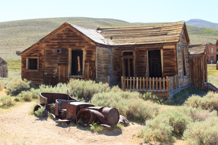 An old, abandoned house sits in a barren, dusty field. The house is made of wood and has a rustic, weathered appearance. In front of the house, there is a pile of old tires and a rusted old carの写真素材