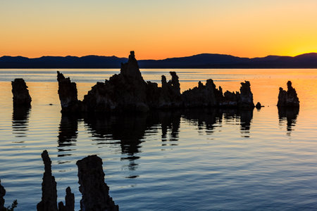 A beautiful sunset over a body of water with a rocky shoreline. The water is calm and the sky is filled with warm colors, creating a serene and peaceful atmosphereの写真素材