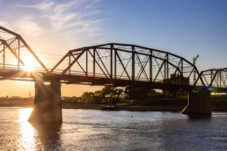 A bridge spans a river with a sun shining on it. The bridge is old and has a rustic appearanceの写真素材