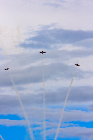 Three fighter jets are flying in formation in the sky. The clouds are white and fluffy, and the sky is blue. Concept of excitement and adventure, as the pilots perform their aerial maneuversの写真素材