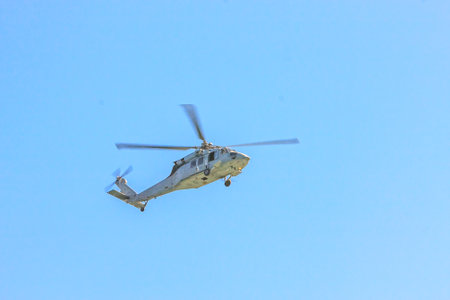 A helicopter is flying in the sky. The sky is clear and blue. The helicopter is in the air and is...