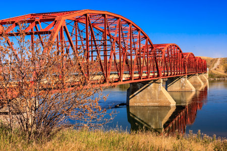A red bridge spans a river, with a reflection of the bridge in the water. The bridge is old and rustic, and the surrounding area is peaceful and sereneの写真素材
