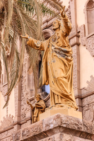 A statue of Jesus is on a pedestal in front of a building. The statue is old and has some damage to itの写真素材