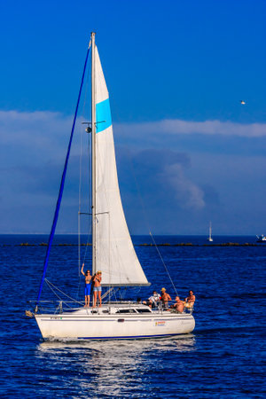 A sailboat with a blue and white sail is sailing on a blue ocean. There are several people on the...