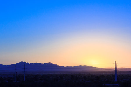The sky is blue and the sun is setting. The mountains in the background are covered in treesの写真素材