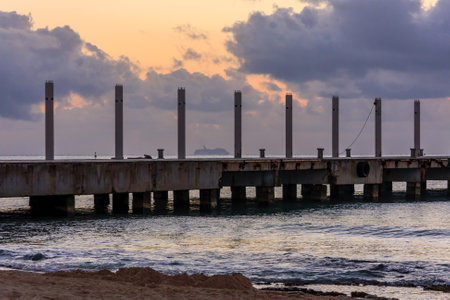 A pier with a boat in the distance. The sky is cloudy and the water is calmの写真素材