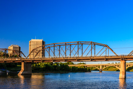 A bridge spans a river with a city in the background. The bridge is old and has a rustic appearanceの写真素材