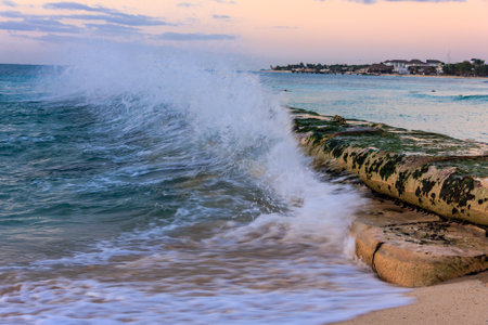 The ocean is crashing against the rocks, creating a powerful and dynamic scene. The water is white and frothy, and the sky is a beautiful shade of pink. Scene is one of awe and wonderの写真素材