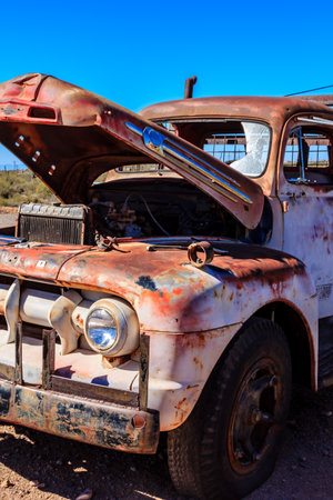 An old rusty truck with its hood open. The truck is parked on a dirt roadの写真素材