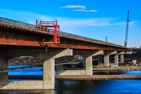 A bridge is being built over a river. The bridge is red and has a crane on it. The crane is in the background and is visible from the bridgeの写真素材