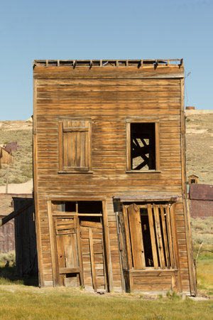A dilapidated old building with a crooked roof and broken windows. The building is surrounded by a...
