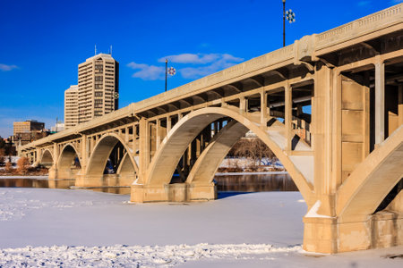 A bridge spans a river with a city in the background. The bridge is made of concrete and is very longの写真素材