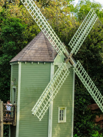 A small green building with a windmill on top. The windmill is old and has a wooden frame. The building is surrounded by trees and bushesの写真素材
