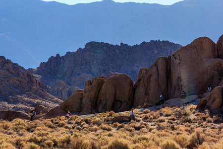 A group of people are sitting on a rocky hillside, enjoying the view of the mountains. The scene is peaceful and serene, with the sun shining down on the groupの写真素材