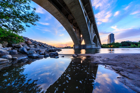 A bridge spans a river with a city in the background. The sky is a mix of blue and orange, creating a serene and peaceful atmosphereの写真素材