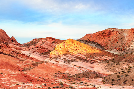 A rocky hillside with a yellow rock in the middle. The sky is blue and the sun is shining