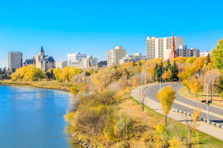 A city with a river running through it and a large building in the background. The city is full of trees and the leaves are changing colorsの写真素材