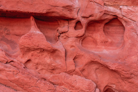 A large, red rock with many holes and indentations. The rock appears to be a part of a cliff or a mountain, and it has a rough, jagged textureの写真素材