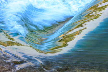A body of water with a wave cresting and a reflection of the wave in the water. The reflection is distorted and blurry, giving the impression of a dreamlike or surreal sceneの写真素材