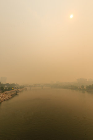 A bridge spans a river with a hazy sky in the background. The sky is a mix of gray and orange,...