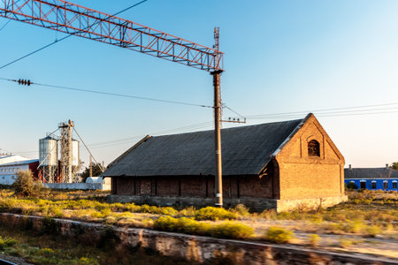 A large brick building with a red roof sits in a field. The sky is blue and the sun is shining