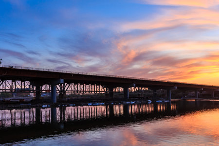 A bridge spans a river with a beautiful sunset in the background. The bridge is made of metal and is surrounded by waterの写真素材
