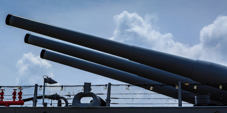 Three large cannons are lined up on a ship. The cannons are black and the sky is blue