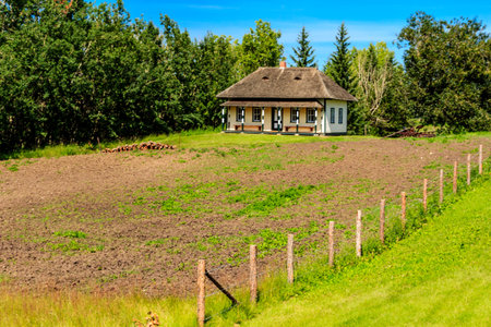 A small house sits on a field of dirt. The house is surrounded by a fence and there are trees in the backgroundの写真素材