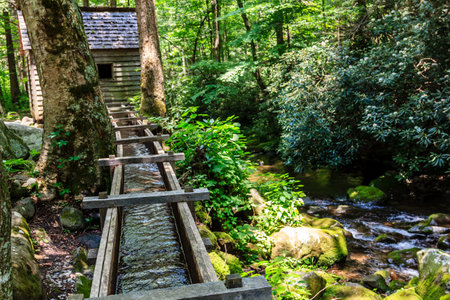 A wooden bridge over a stream with a cabin in the background. The cabin is surrounded by trees and the stream is clear and calm. The scene is peaceful and serene, with the cabinの写真素材