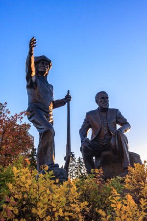 Two statues of men, one of them holding a gun, are sitting on a hillside. The other statue is standing and pointing to the sky. The scene is set against a backdrop of a blue skyの写真素材
