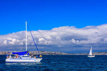 A blue and white sailboat is sailing in the ocean. The sky is clear and blue, and there are no clouds in the skyの写真素材