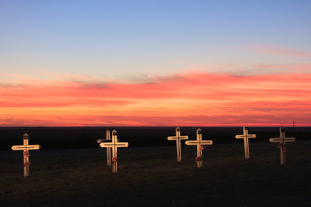 A row of crosses are standing in a field at sunset. The sky is a beautiful mix of orange and pink huesの写真素材