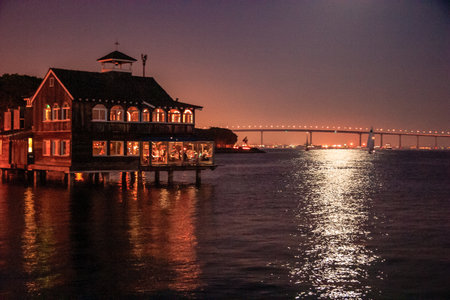 A house with a bridge in the background. The water is calm and the sky is dark. The house is lit up at nightの写真素材